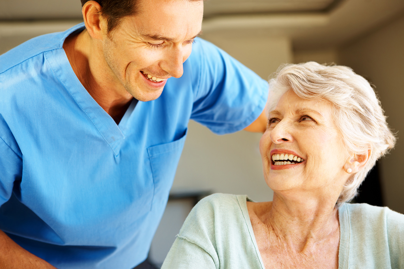 A smiling senior woman and a smiling caregiver offering her assistance.